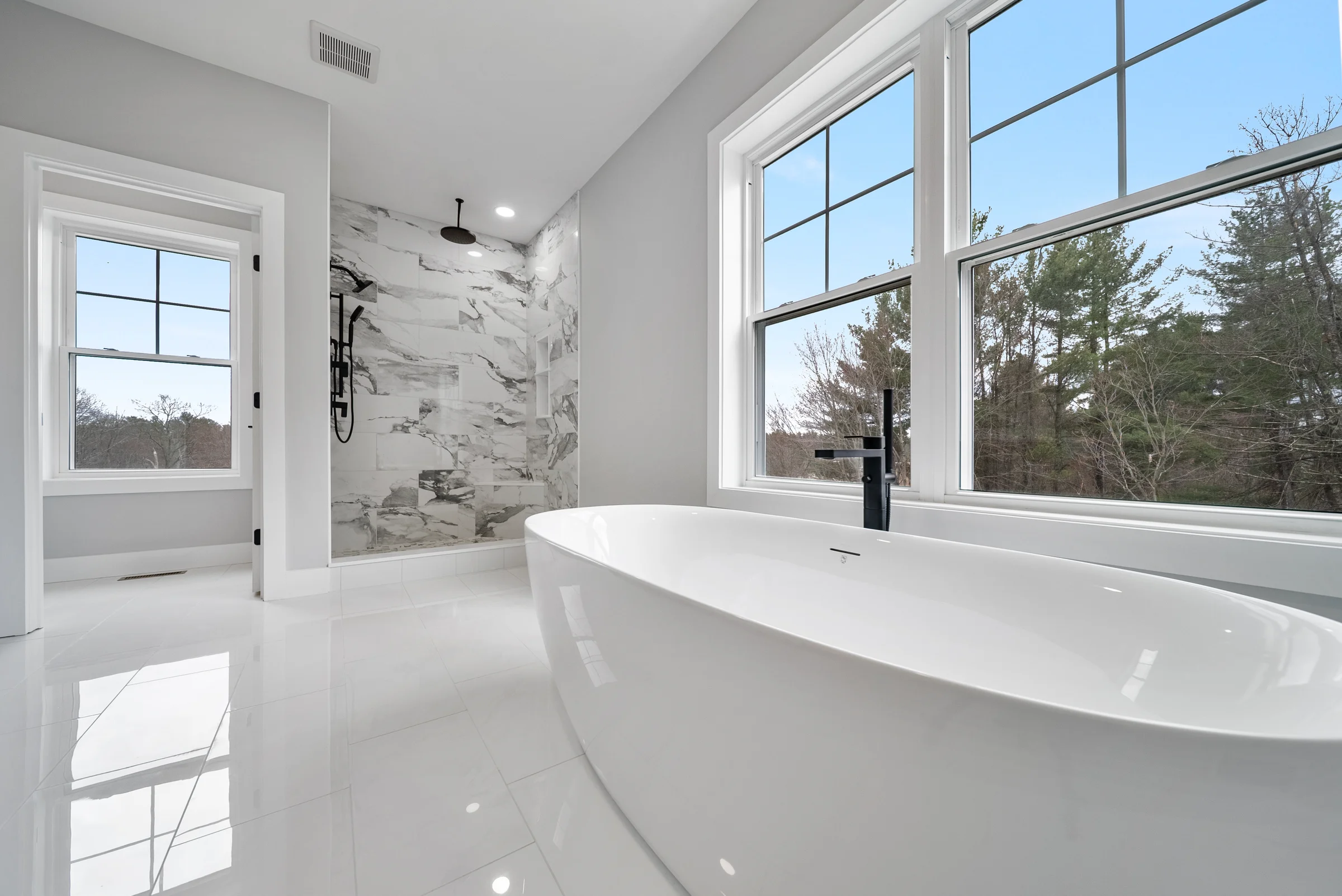 Primary bath with a freestanding tub against a wall of windows, marble shower and polished tile carrying the daylight across the floor