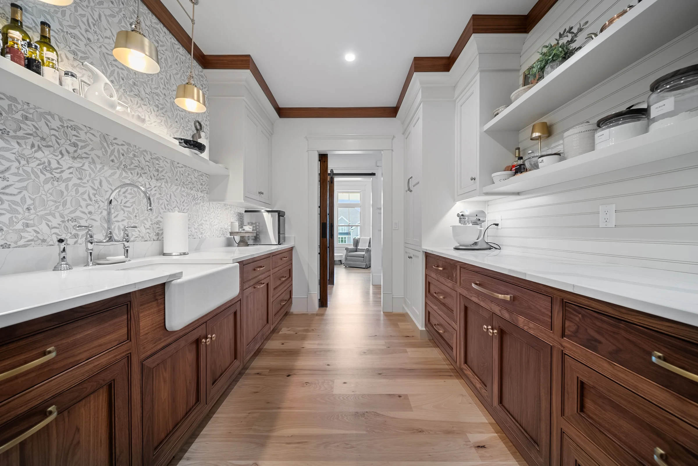 Walnut butler's pantry receding to a doorway, quartz counters and floating shelves running both walls under brass pendants