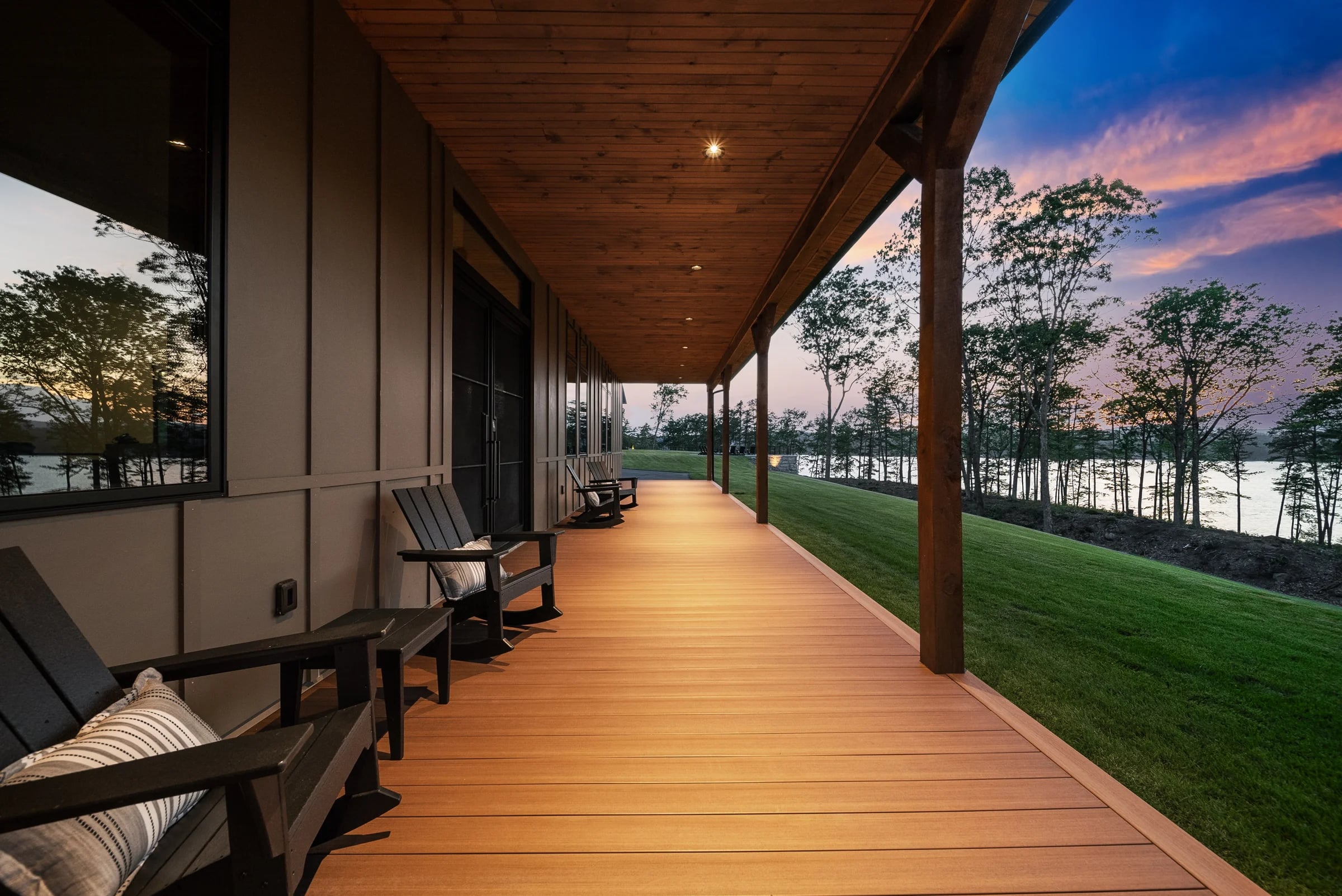 Covered porch running to a vanishing point, warm deck lighting and rocking chairs receding toward the lake at sunset