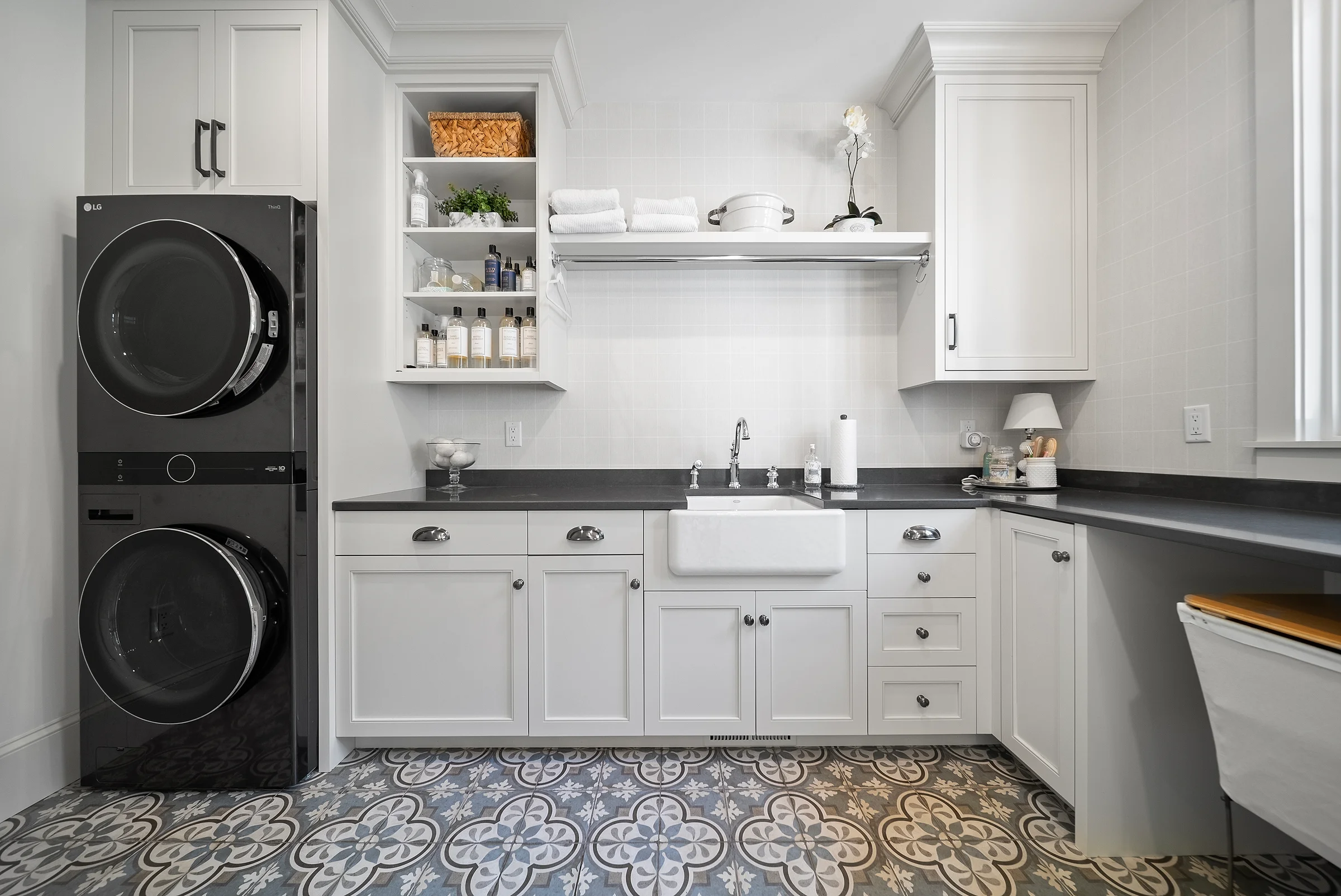 Laundry and utility room in white cabinetry with a stacked washer-dryer, open shelving and a farmhouse sink over patterned encaustic tile