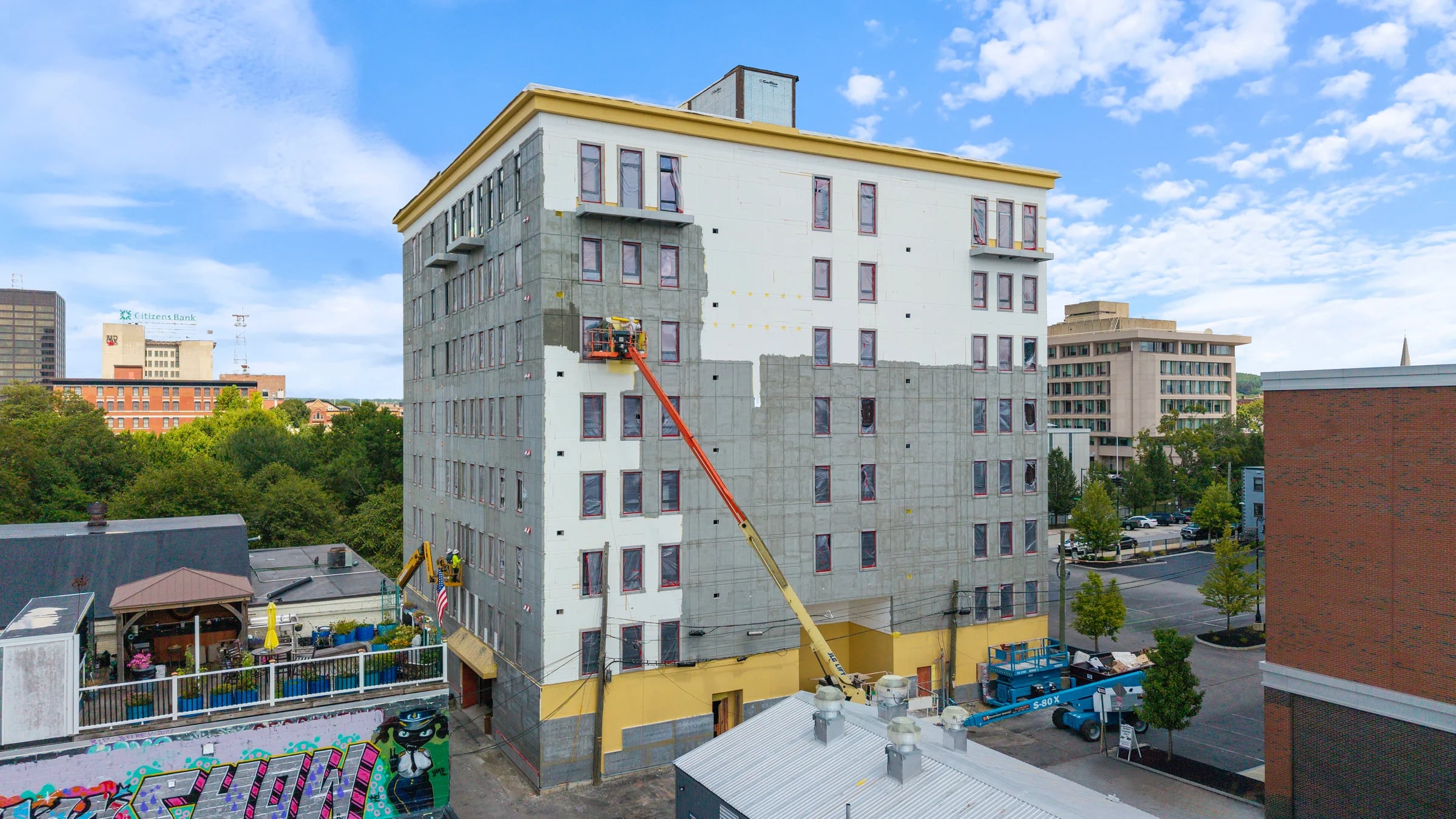 Seven-storey downtown mid-rise mid-renovation, a boom lift raised to the upper facade with a worker in the basket and a scissor lift at street level