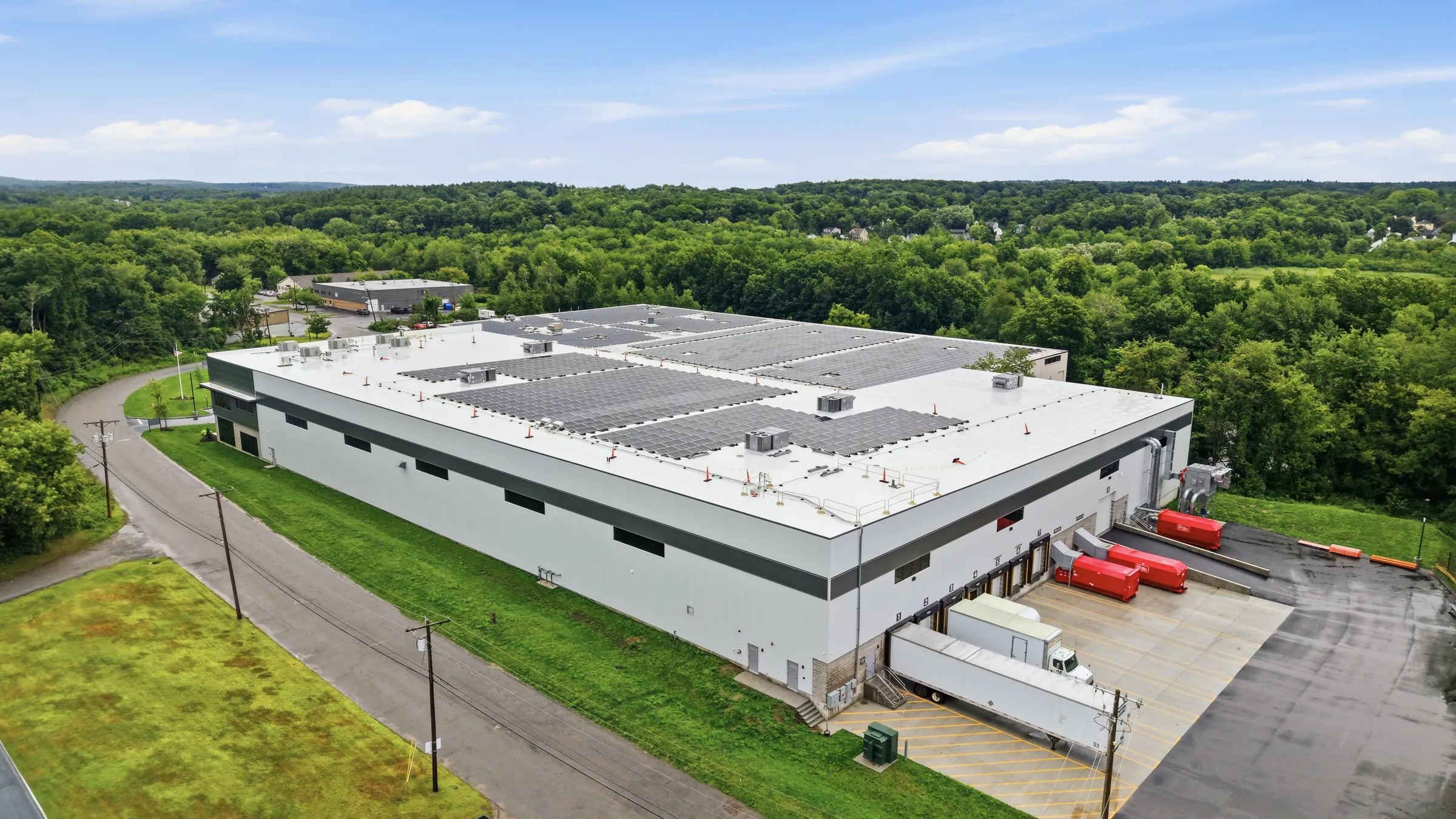 An aerial view of a warehouse with solar panels across its roof and red trailers backed into the loading docks