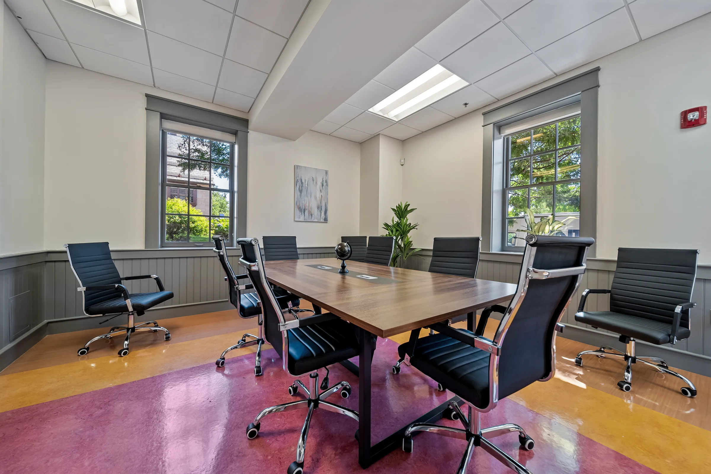 A conference room with a long wood table and black chairs, lit by windows on two walls