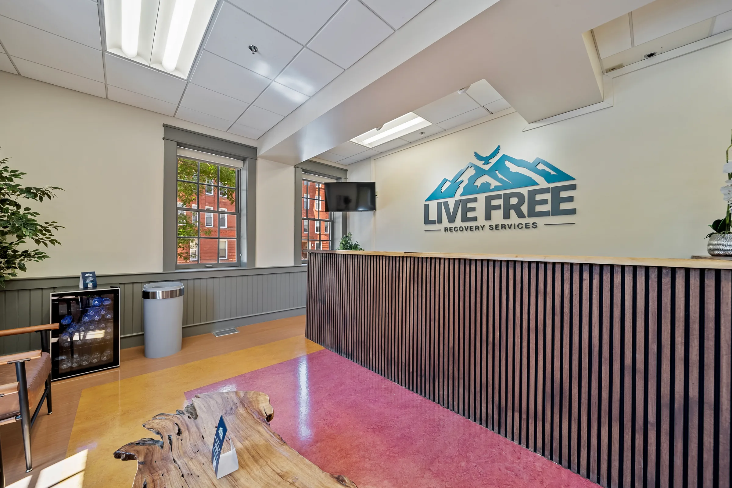 A reception desk with a live-edge wood top and slatted front, beneath a logo painted on the wall