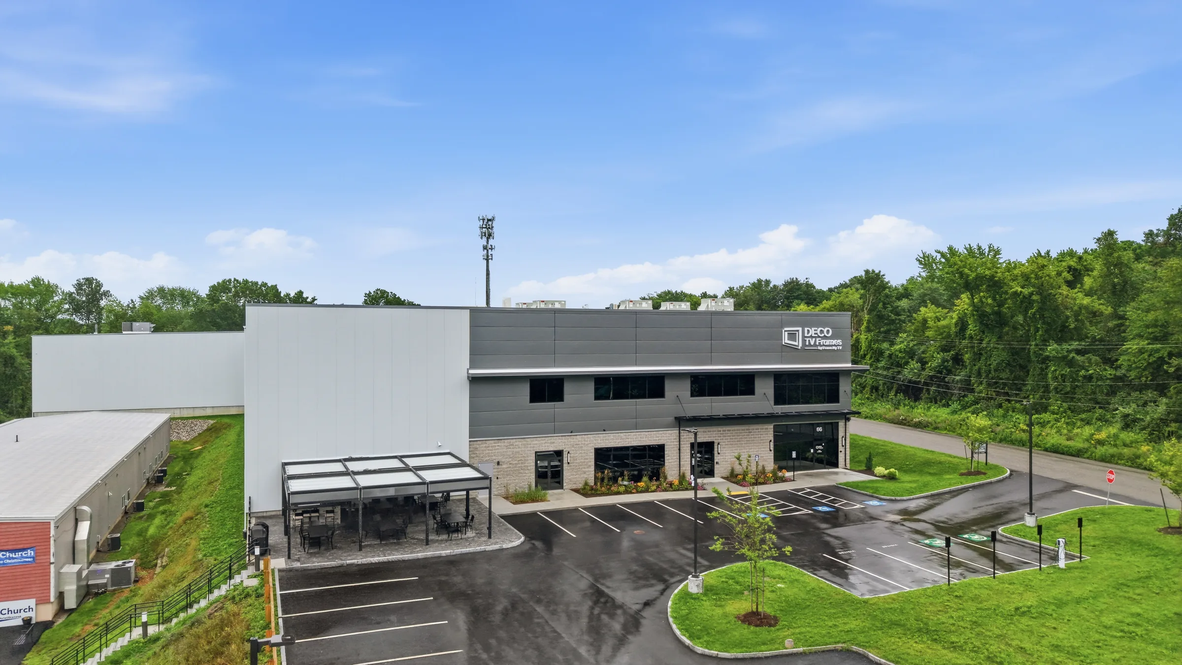 A modern grey and white office block fronting a manufacturing plant, with a covered patio and fresh parking