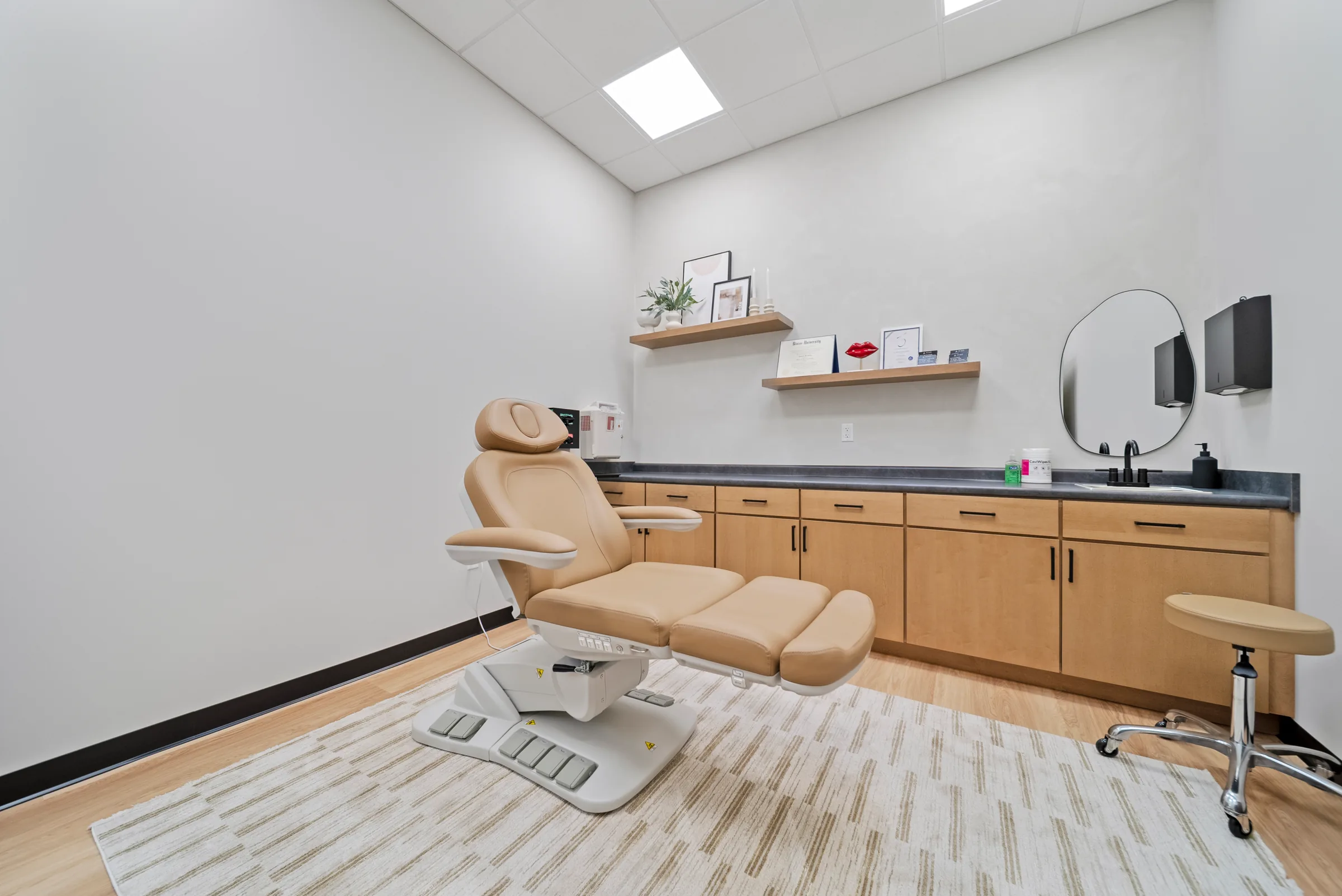 A treatment room with a tan reclining chair, a round mirror, and light oak cabinets along one wall