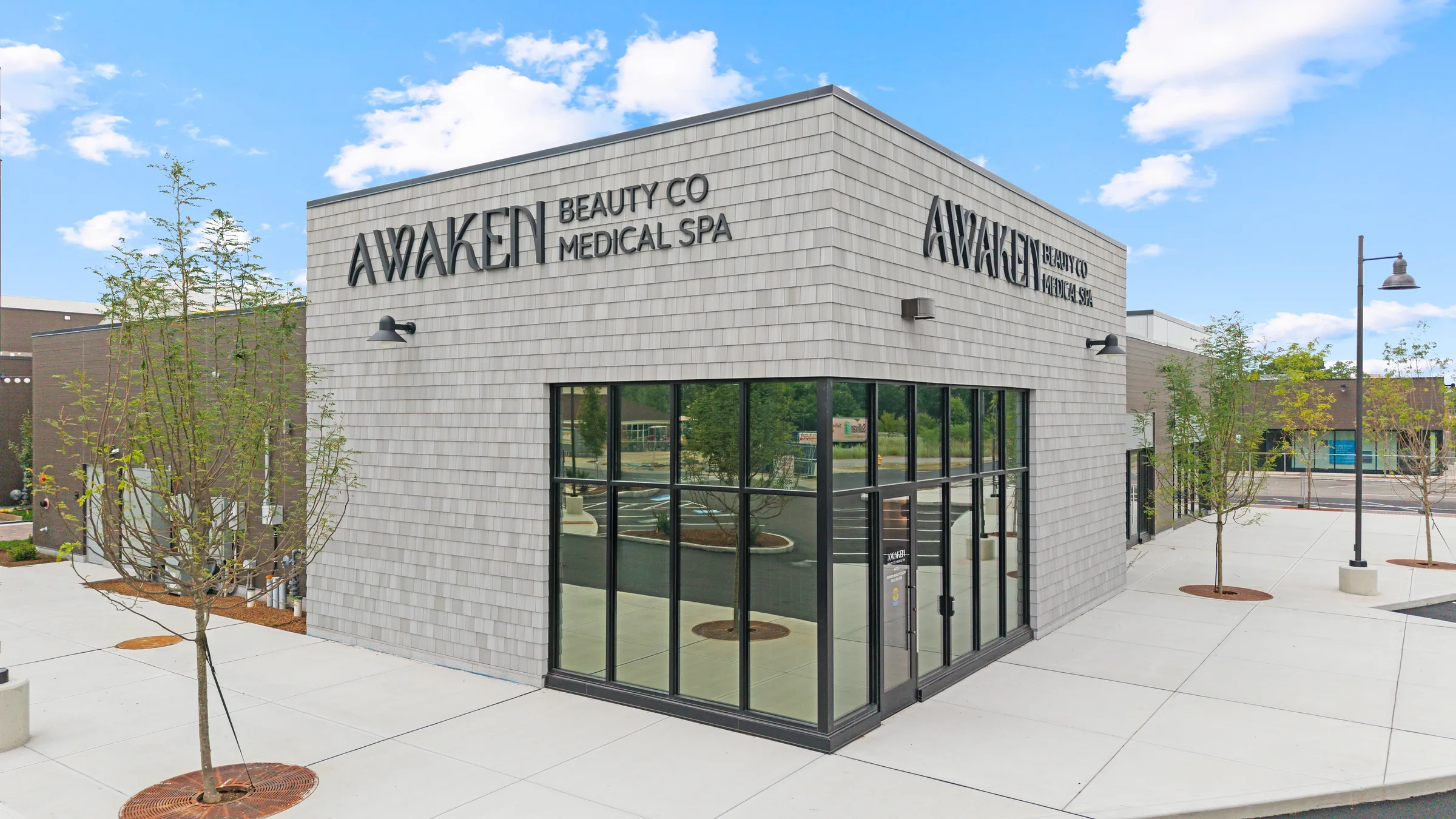 A grey-shingled medical spa shot from just above the sidewalk, its name lettered across both street-facing walls above a glass corner entry