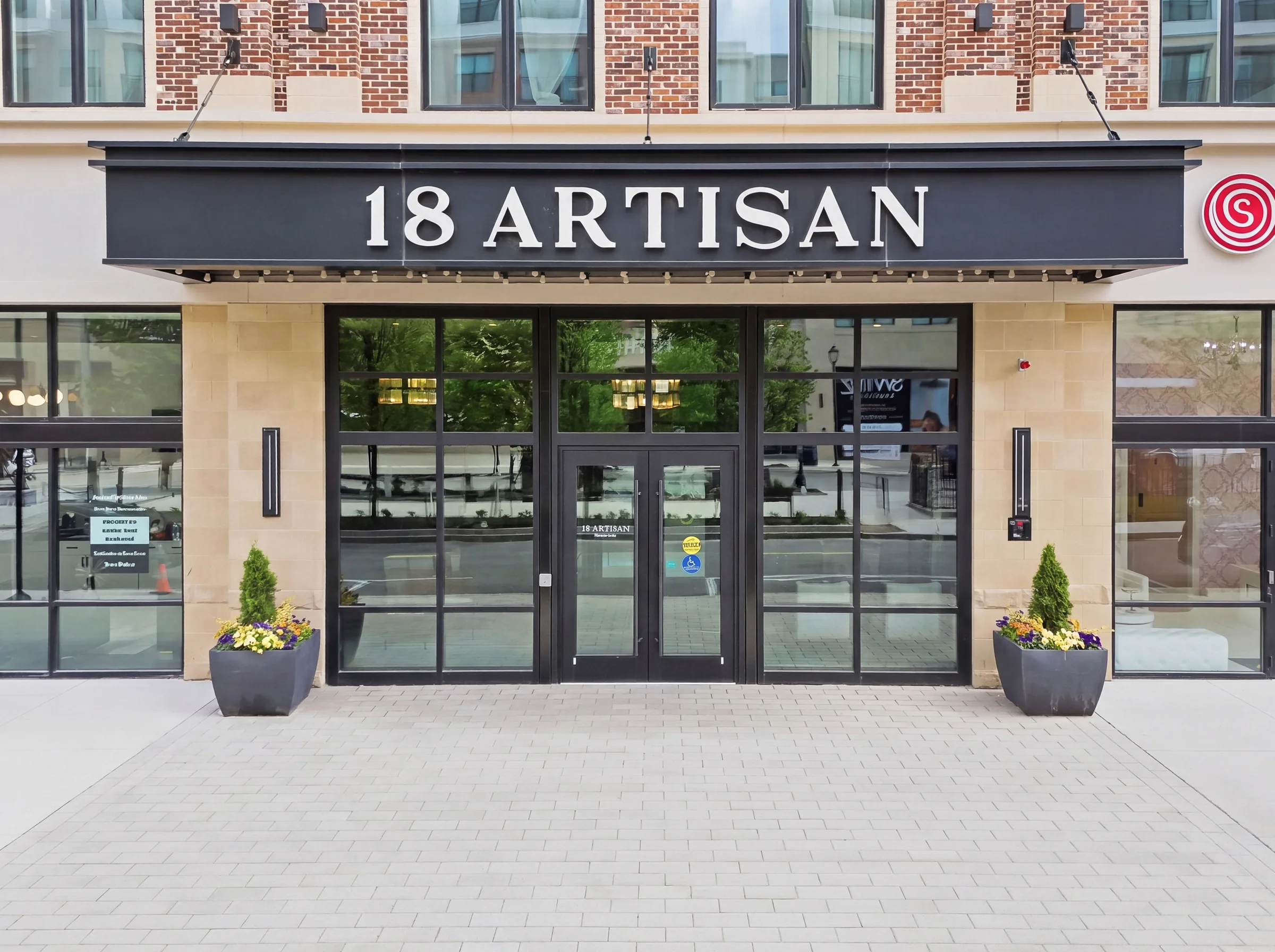 A brick and cast-stone commercial building entrance, a dark awning over glass doors with planters either side