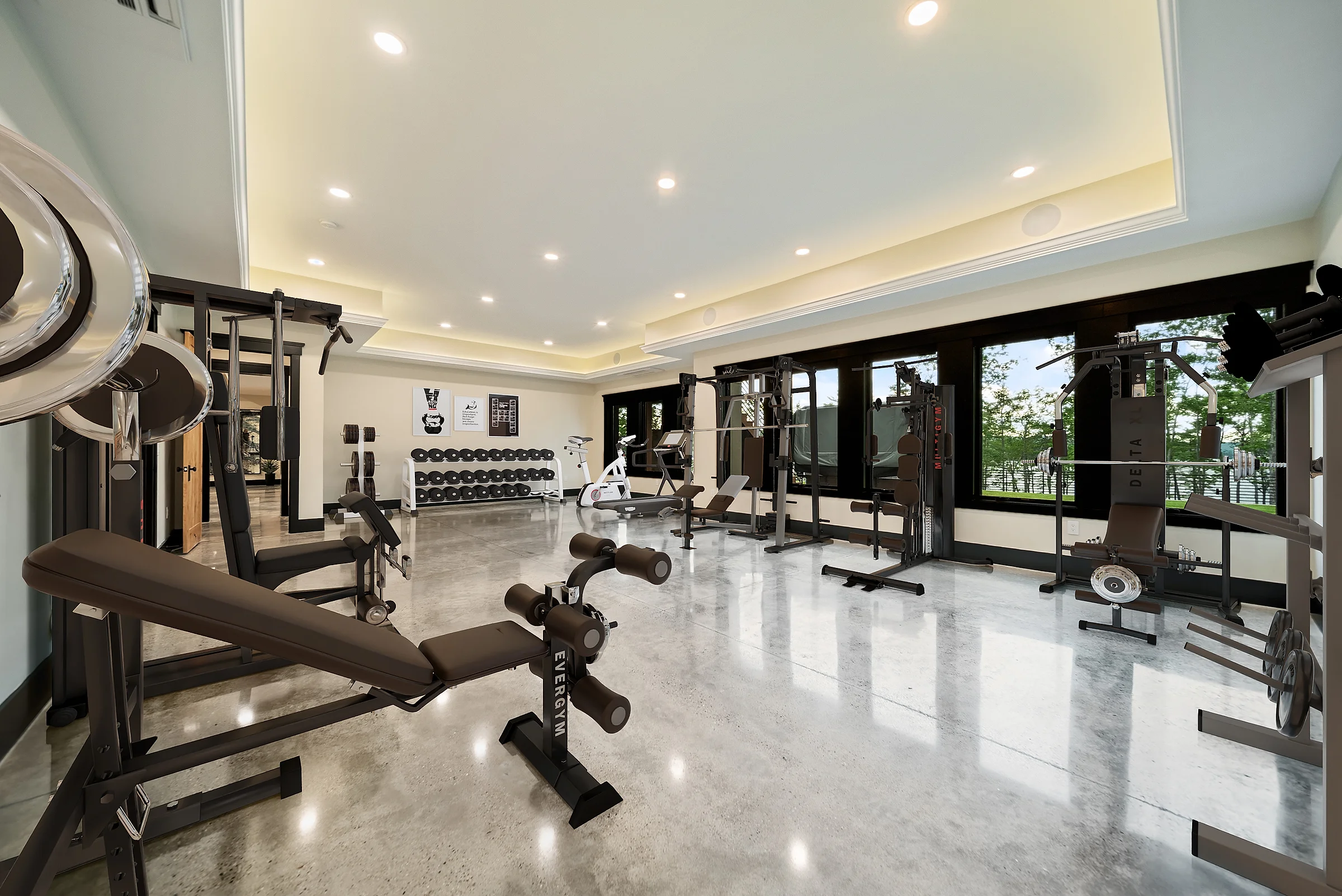 Fitness room on polished concrete with racked free weights and cable machines along a wall of windows