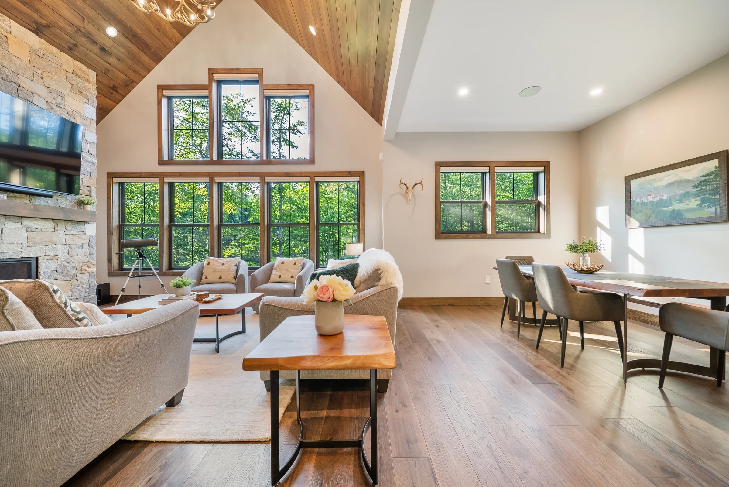 A vaulted great-room lounge with sofas and a dining area beneath forest-view windows
