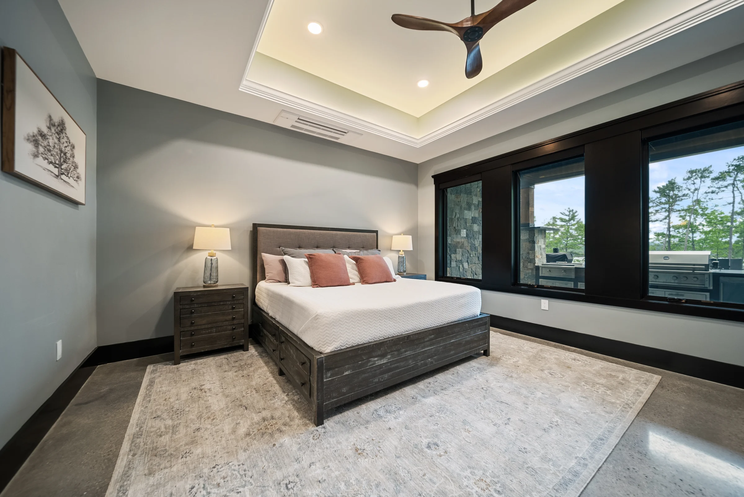 A styled guest bedroom in soft grays with a tray ceiling and large windows