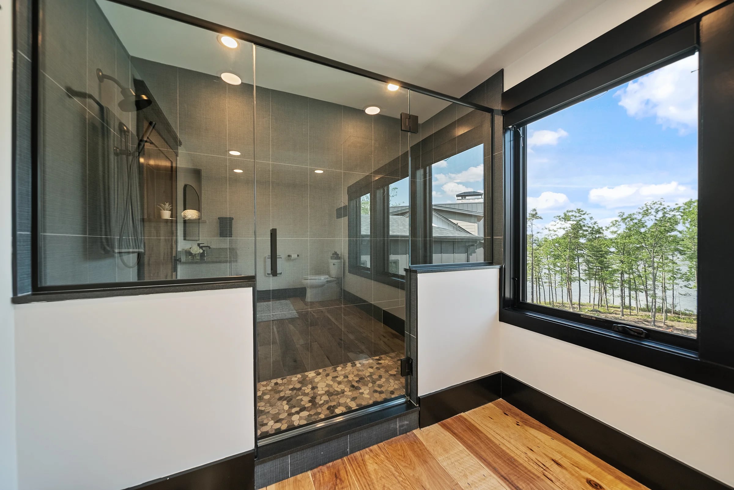 Spa bath behind full-height glass, river-rock floor and a walk-in shower open to a wall of windows over the lake