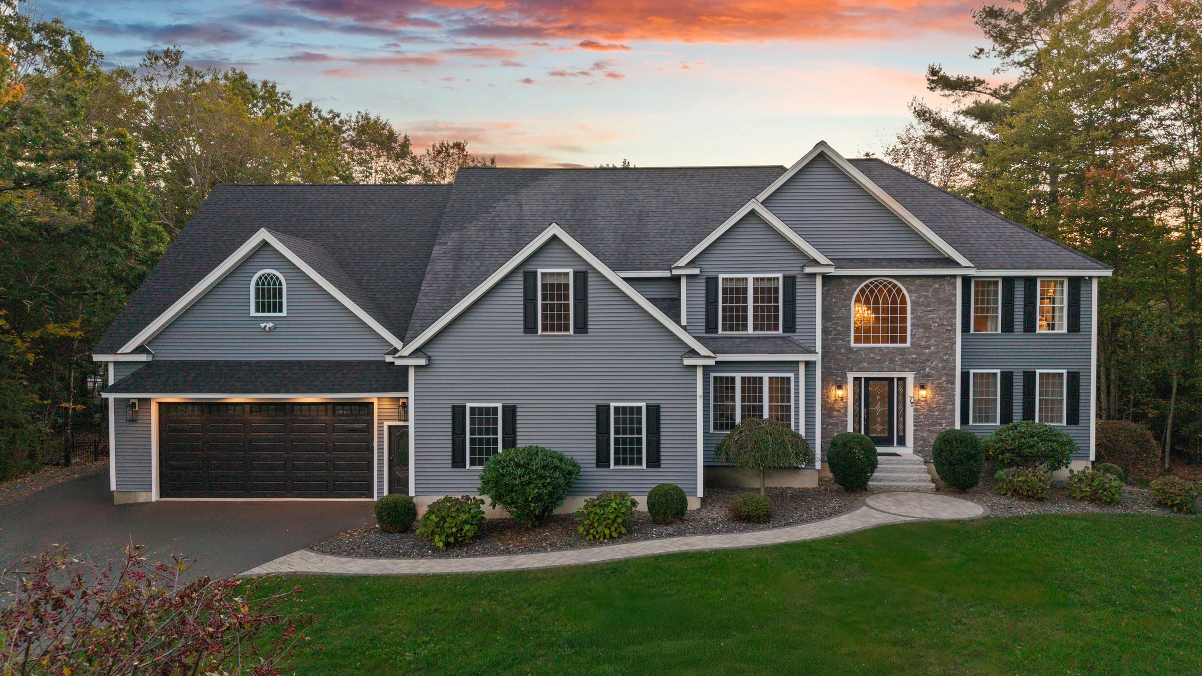Dusk exterior of a grey colonial in Hampstead, NH, windows lit