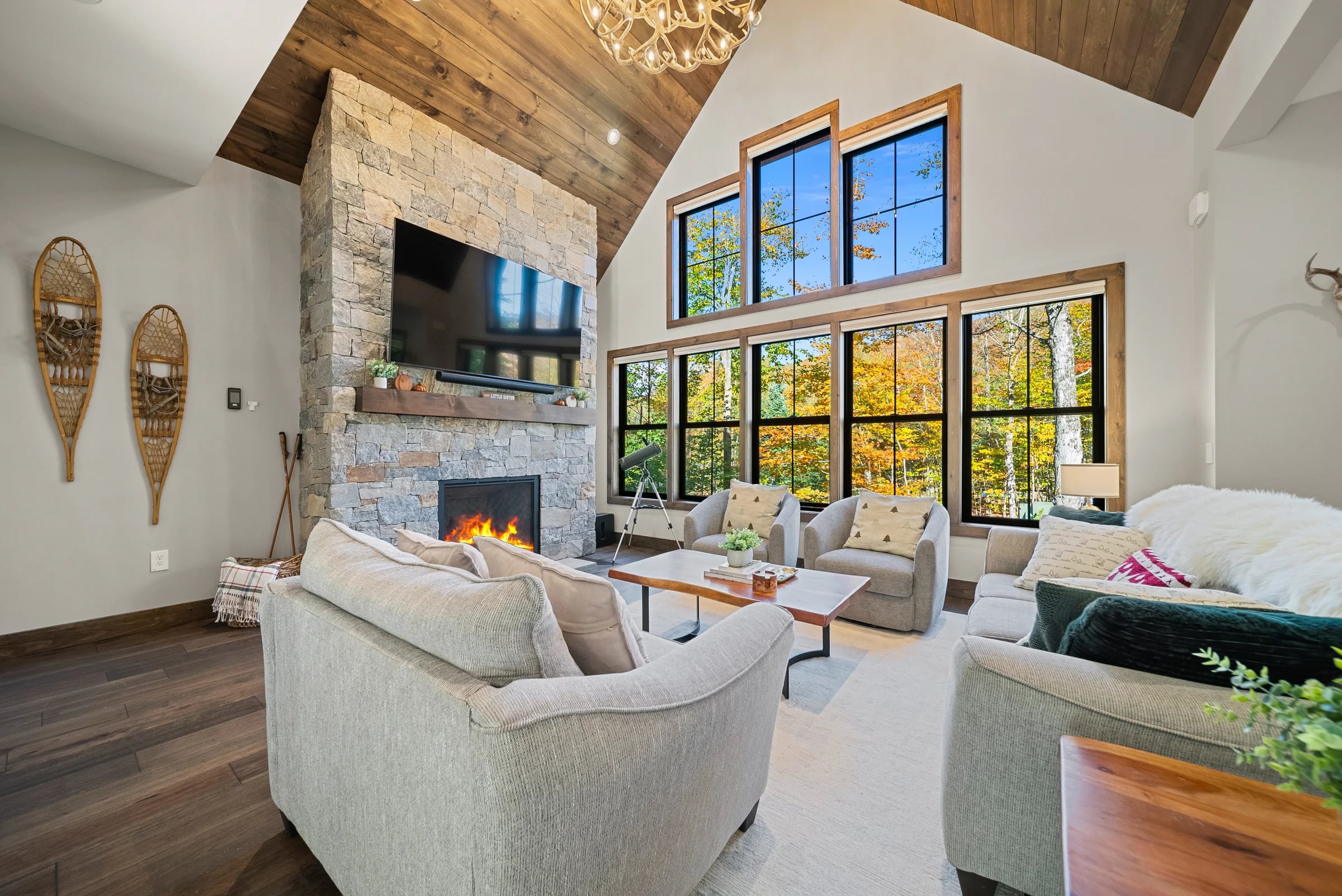 Cozy living room with a stone fireplace, sectional seating, and forest-view windows