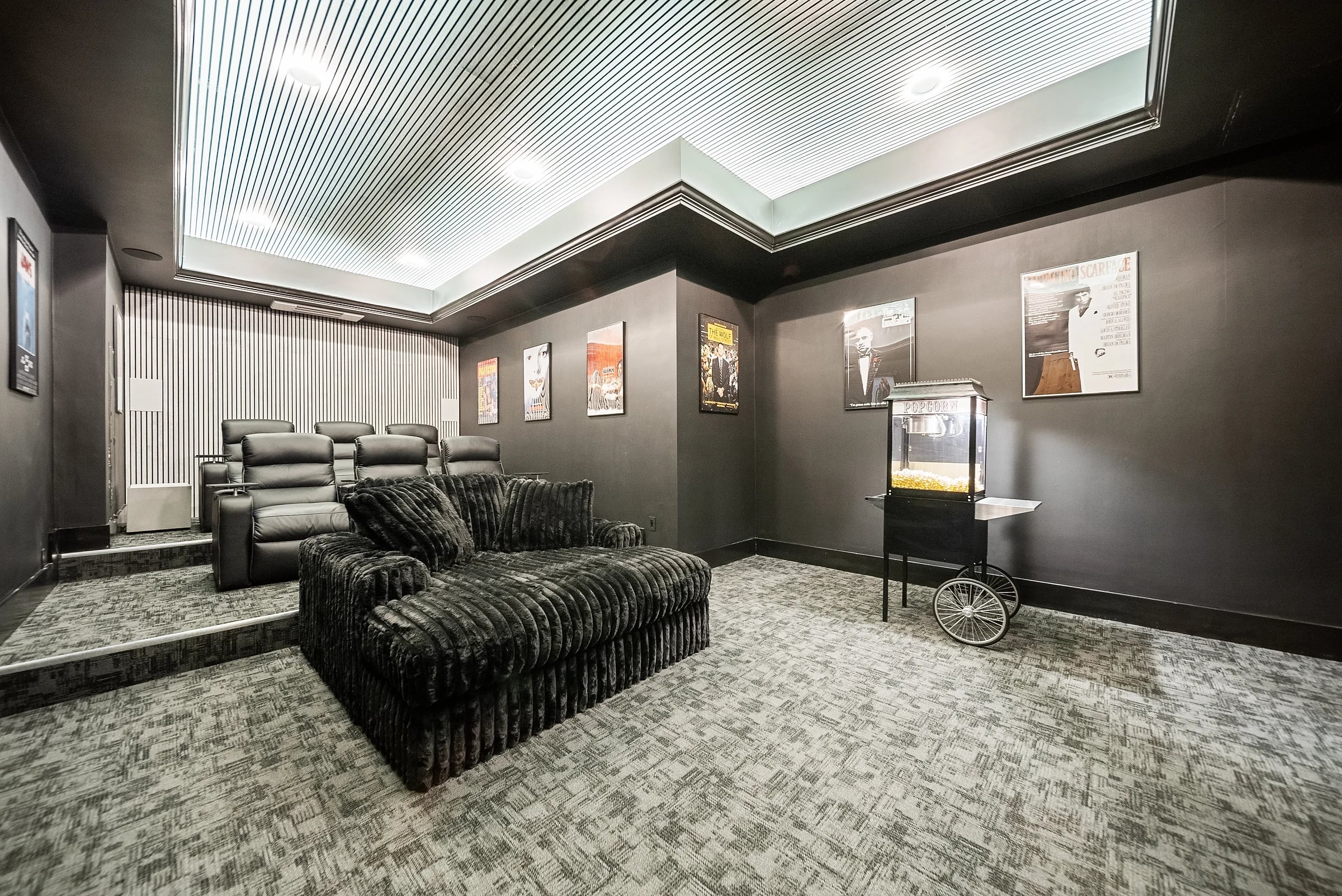 Home theater in charcoal with tiered leather recliners, a backlit coffered ceiling and a popcorn cart by the wall