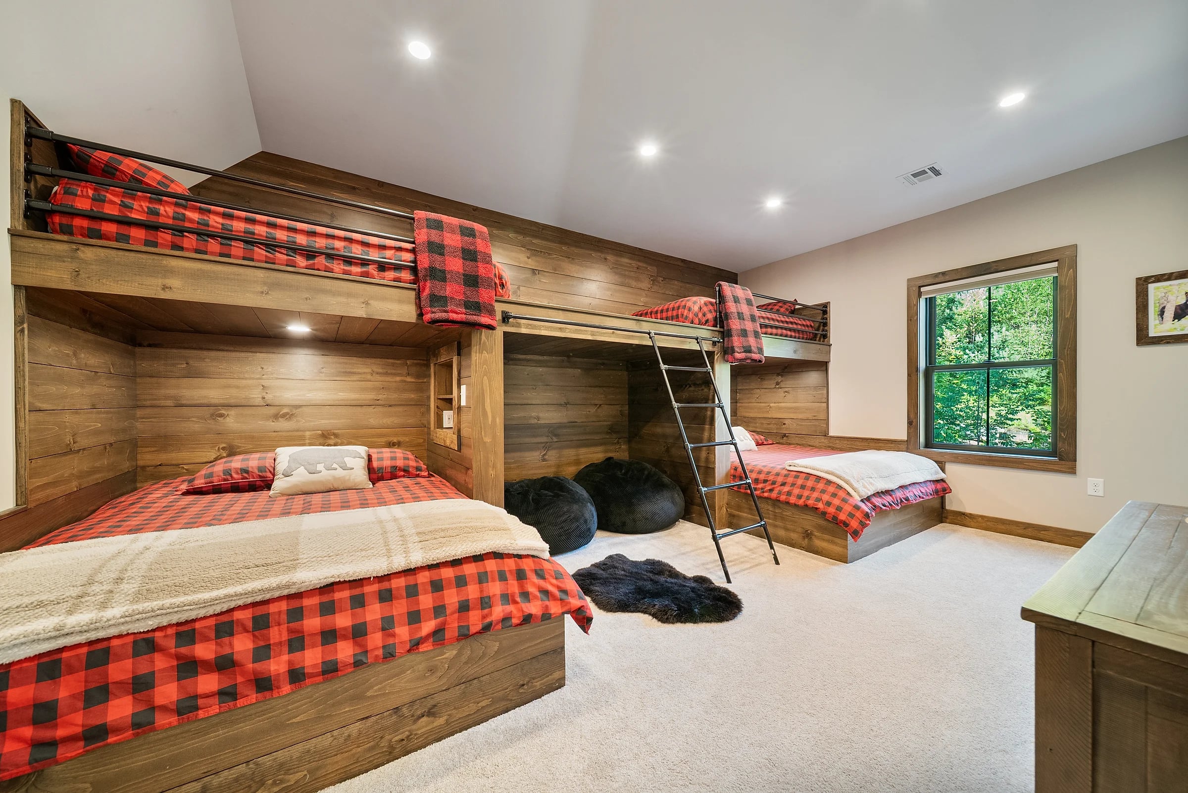 Bunk room in knotty pine with built-in bunks in buffalo-check bedding and a forest view through the window